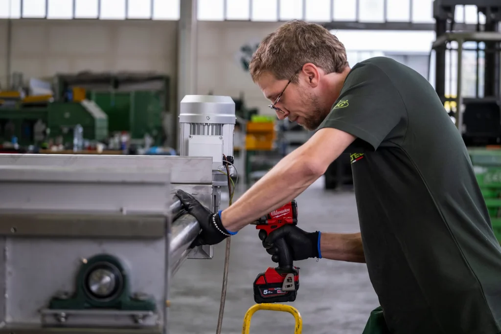 Tecnico che serra con avvitatore a batteria il telaio in acciaio inox di una linea, con motore elettrico e cuscinetto